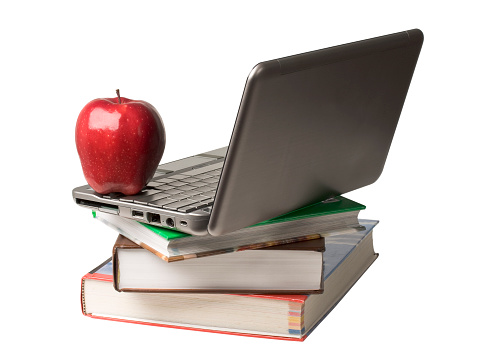 Red apple sitting on top of computer and books isolated on white background.