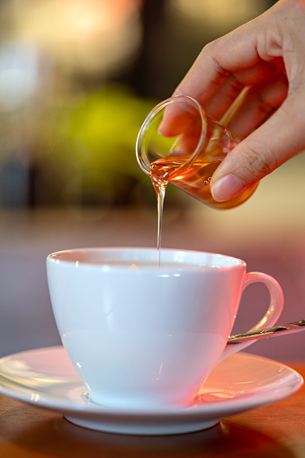 Close-up of a woman's hand pouring pure honey into a cup of lemon tea.