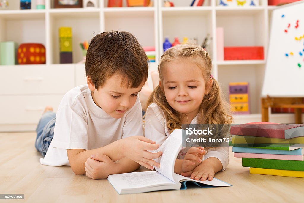 Scuola ragazzo insegnando e mostrando la sua sorella come leggere - Foto stock royalty-free di Allegro