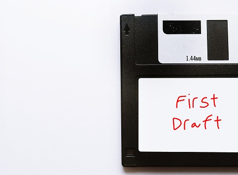 Vintage floppy disk with handwriting label FIRST DRAFT on copy space white background- concept of writing process, very first version of writing piece, script, book or novel