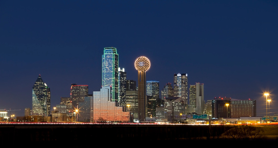 Panoramic shot of Dallas, Texas business district showcasing skyscrapers glowing and lights glimmering at night.