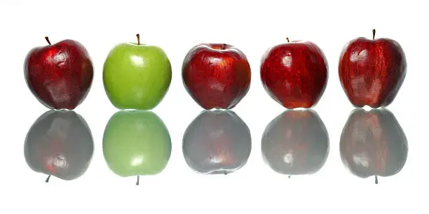 A green apple being standout among red apples isolated on white background.