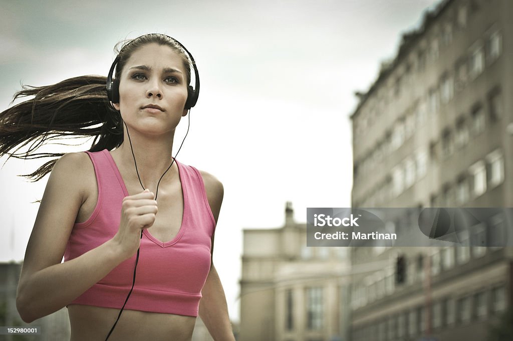 Young person listening misic running in city street Person (young beautiful woman) listening music running (jogging) in city street Active Lifestyle Stock Photo