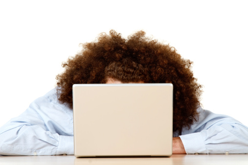 Long frizzy or afro style hair of person working on open laptop computer; white studio background.