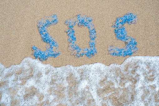 The world SOS made of pieces of plastic washing away by the wave on a sandy sea beach. Help the planet.