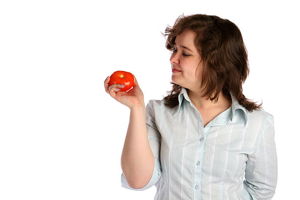 Chubby girl in white shirt demonstrates tomato. stock photo