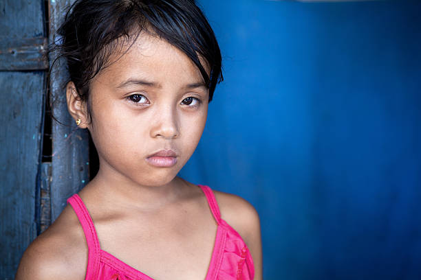 Young Filipina girl 8 years old with sad and somber expression over blue, poverty in the Philippines.