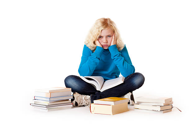 Schoolgirl sitting tired, frustrated on floor learning with study books stock photo