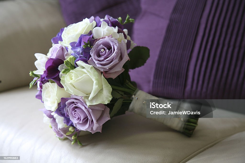 Bouquet of flowers with purple theme a bouquet of flowers, could be from a wedding, lays on a sofa. the colour theme of the flowers is purple and there is a purple cushion on the sofa Bouquet Stock Photo