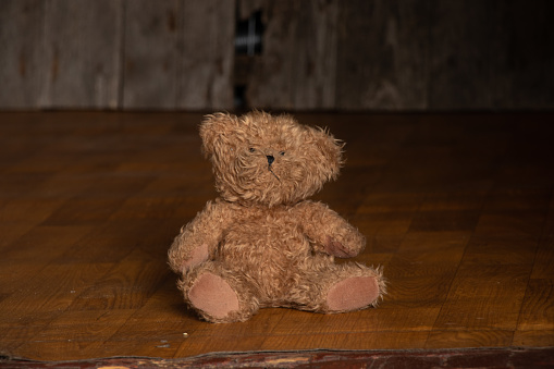 old dirty teddy bear lies on the floor in a dark room at home, abandoned and alone, poverty