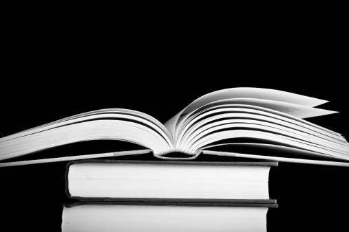 This is a high contrast shot of an open books sitting on a stack of books. Shot in black and white on a black background.