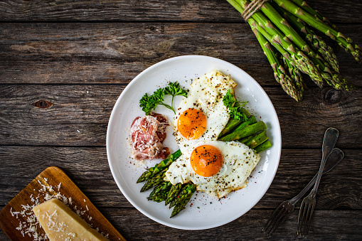 Sunny side up eggs with asparagus and parmesan on wooden background