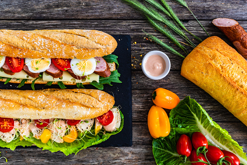 French-style baguette - baguette with sausage, roasted chicken meat, boiled sliced eggs and fresh vegetables on wooden table