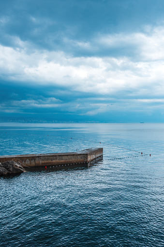 Concrete stone pier at town of Lovran in Kvarner gulf of Adriatic sea at sunset with overcast stormy sky