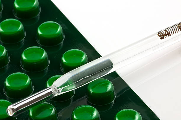 Green pills in capsules and thermometer stock photo