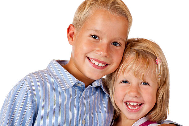 Close up of cute boy and girl siblings smiling looking at camera and embracing as they wait at an elevated covered city train stop on a cold day.