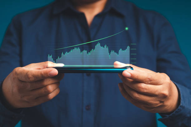 istock Hand holding of a mobile phone with digital increasing bar business graph growth 1529985676