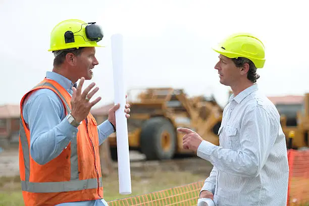 Photo of Two construction workers arguing on either side of a pole