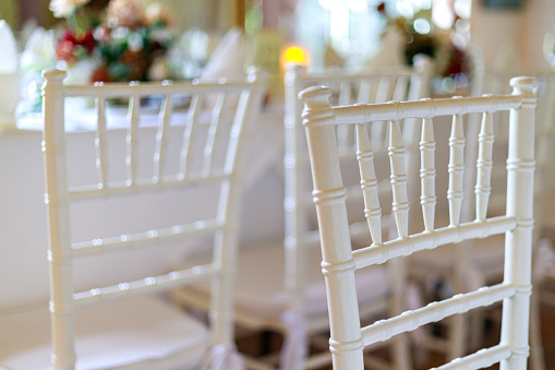 White wedding chairs are arranged in a reception hall close up