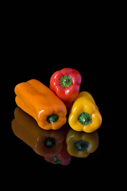 Orange yellow and red baby sweet peppers with reflection against black background