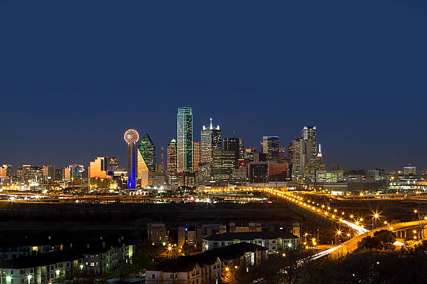 Wide-angle shot of Dallas, Texas business district showcasing skyscrapers glowing and lights glimmering at night.