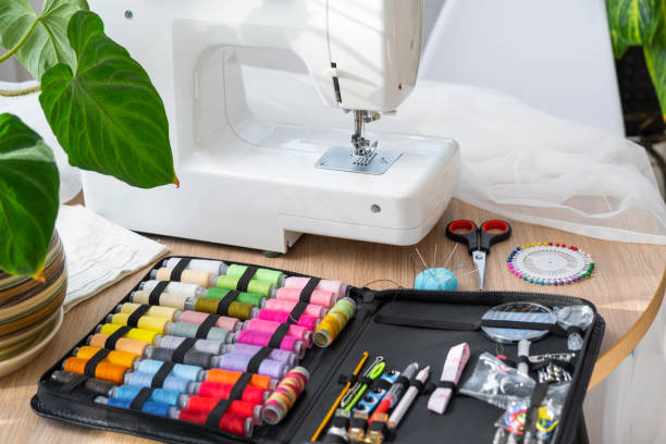 istock Sewing layout with multicolored spools of thread close-up, needles, electric sewing machine. Filling the thread into the sewing needle, adjusting the tension. hobby, home business 1530007441
