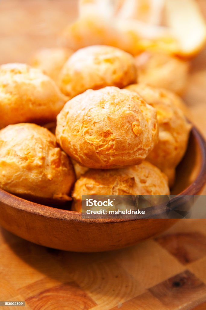 A wooden bowl filled with multiple cheese gougeres Freshly made cheese gougeres on wood cutting board Gougere Stock Photo