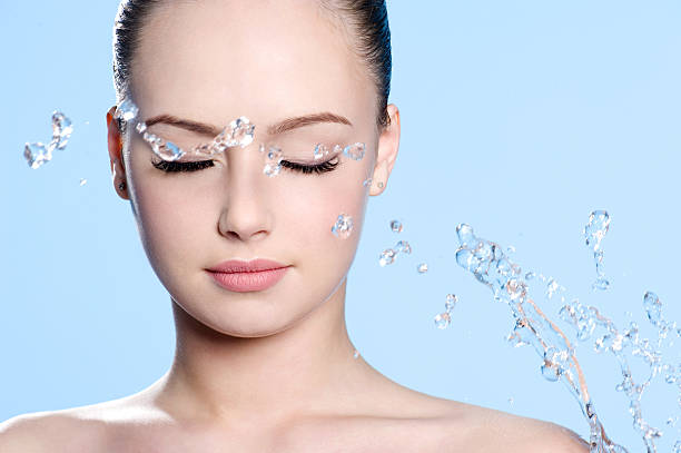 Beautiful young clean female face with splash of water - blue background