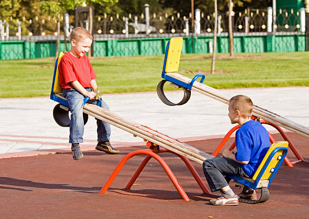 Two young boys on a seesaw in the park stock photo