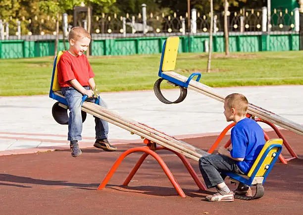 Boys playing on a seesaw on a playground in a sunny day