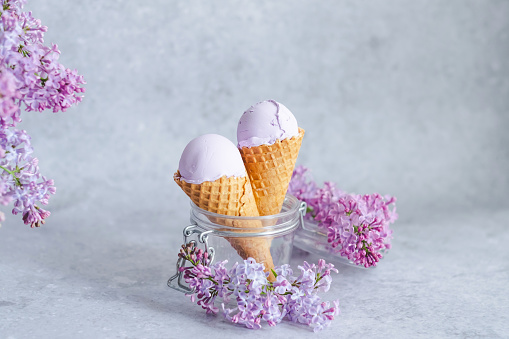 Creamy ice cream in cones decorated with lilac flowers on a gray background. Filipino ice cream. Healthy vegan dessert