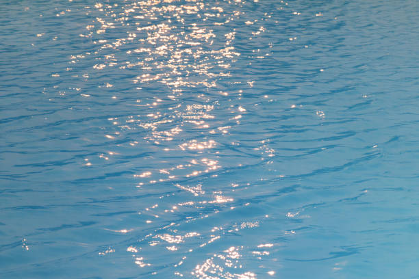 Blue water with ripples on the surface. Defocus blurred transparent blue colored clear calm water surface texture with splashes and bubbles. Water waves with shining pattern texture background.