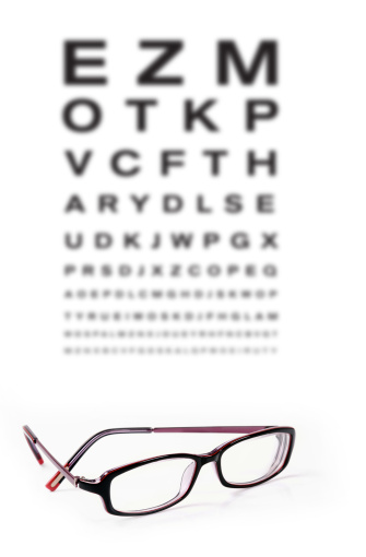 Eye test chart out of focus on white with glasses in foreground