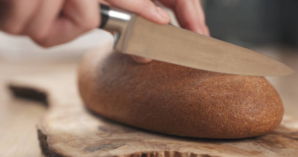 まな板の上でライ麦小麦の素朴なパンをスライスする若い女性の手 - brown bread bread cutting board full length ストックフォトと画像