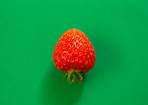 Single strawberry isolated on a green background with copy space. Top view, flat lay.