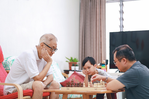 Three generations of family enjoy each other's company over a chess board game at home
