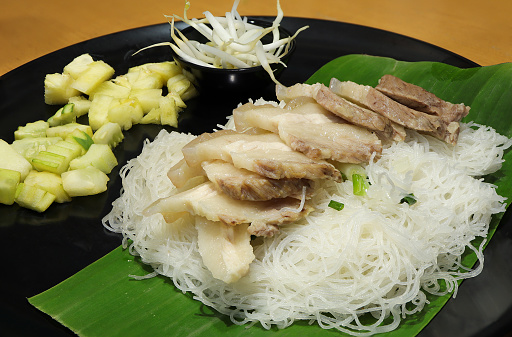 Banh Hoi, Vietnamese rice noodles bundled with grilled pork, cucumbers and fresh herbs on black plate. Vietnamese cuisine