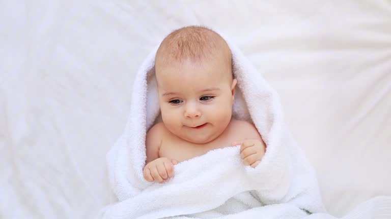 Six month baby wearing towel after bath. Childhood and baby care concept, cute little newborn baby in white towel after bathing