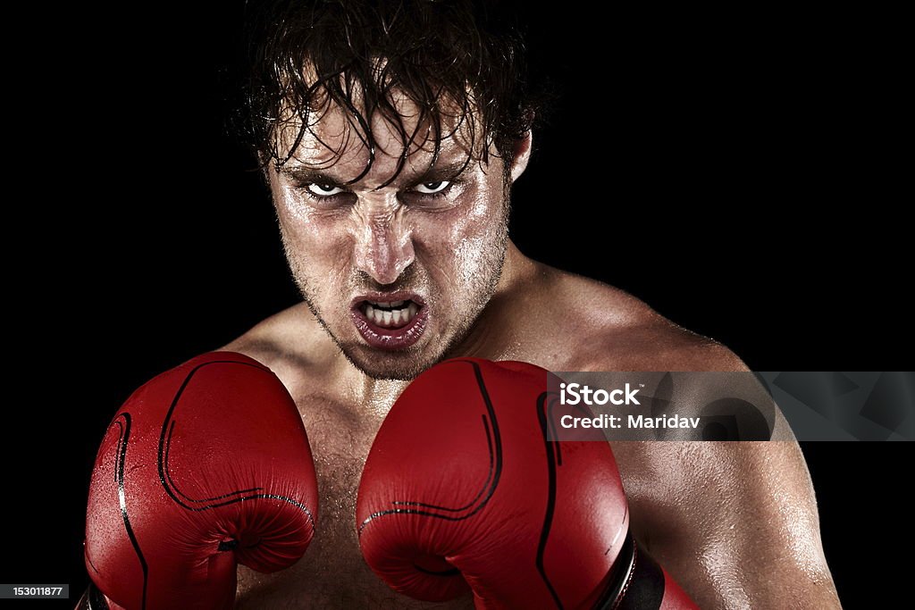 Boxer Boxing Boxer Boxing staring angry, mean and sweaty showing strength. Young man looking aggressive with boxing gloves. Caucasian male model isolated on black background. Boxing - Sport Stock Photo