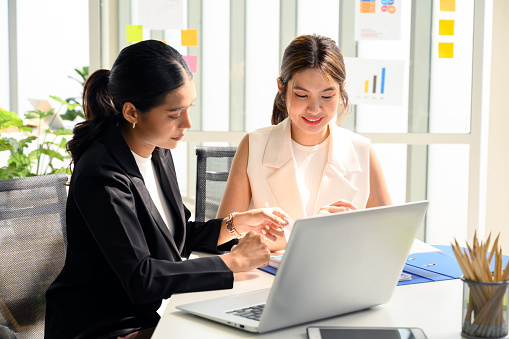 Two young Asian businesswoman in smart casuals read some documents, making plans together. Business people talking together with documents at office