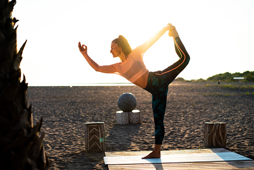 Woman exercising Yoga on the beach at sunset