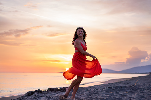 Happy woman in red dress spinning at the beach during summer