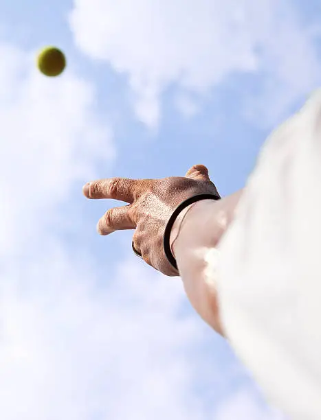 Tennisplayer trowing up a ball with his hand to serve blue sky