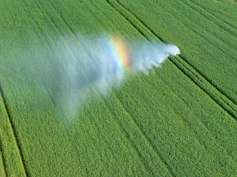Irrigation of a green field in sunlight with a rainbow reflection in the water vapor. Västergötland, Sweden.