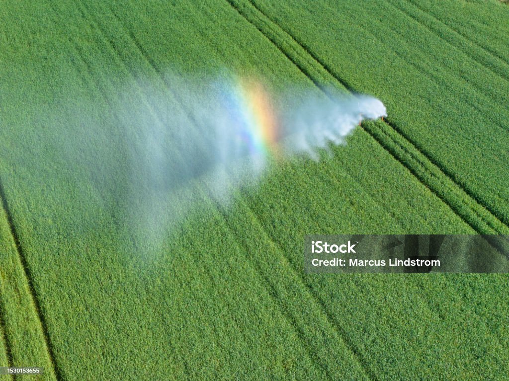 Irrigation of a field in sunlight Irrigation of a green field in sunlight with a rainbow reflection in the water vapor. Västergötland, Sweden. Agriculture Stock Photo