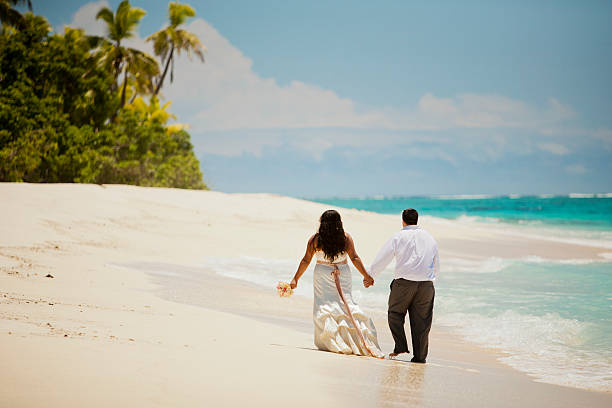 Fijian newlyweds strolling on beach Multi-Ethnic newlywed couple walking on Fijian beach. Facing away from camera. Dressed in wedding attire. taveuni stock pictures, royalty-free photos & images