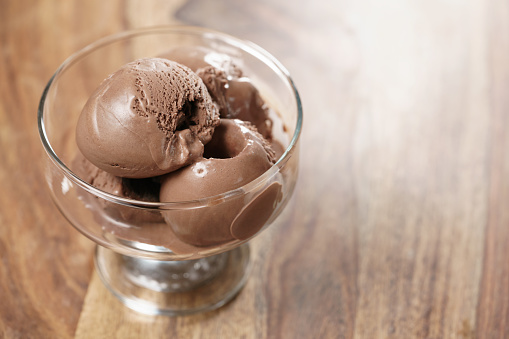 chocolate ice cream in glass bowl on wooden table, shallow focus