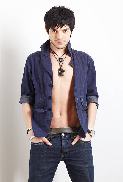 Portrait of young handsome brunet man in shirt and jeans posing on gray wall