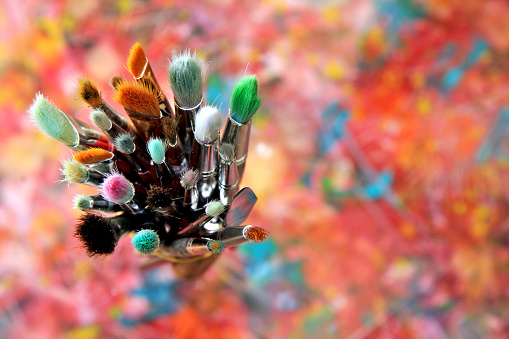 looking down onto a collection of used artists paint brushes sitting on an original abstract canvas