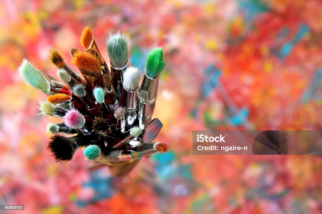 artist brushes looking down onto a collection of used artists paint brushes sitting on an original abstract canvas Art Class Stock Photo